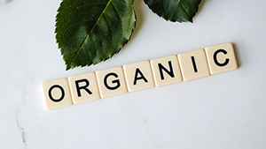 ORGANIC spelled out in letter tiles on a white marbled background with green leaves at the top
