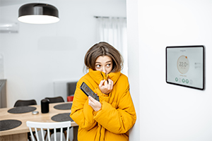 Girl in yellow coat indoors staring at smart thermostat with phone in hand getting ready to call for Manasquan heating repair